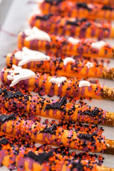 Dipping pretzel rods into melted chocolate to make Halloween chocolate-covered pretzel rods.