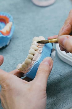 Close-up view of a dental technicians hands holding a toothbrush, focusing on manufacturing prosthesis using dental materials and tools for oral care. Vertical photo.