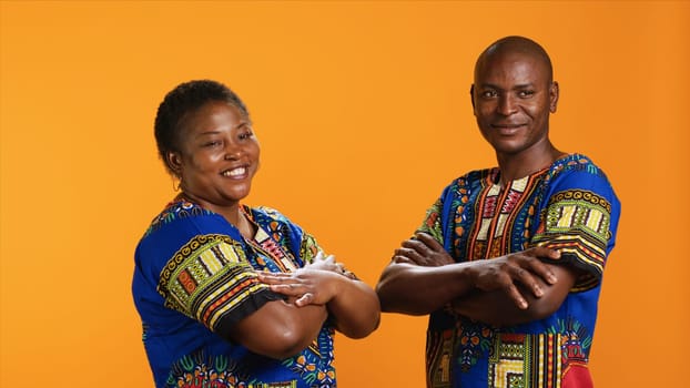 African american couple in traditional attire posing on camera, feeling confident with their lifestyle and culture. Smiling man and woman standing in studio, wearing colorful clothing.