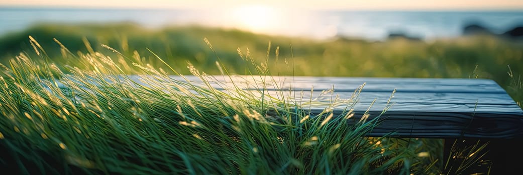 A wooden bench is sitting in a field of tall grass. The grass is blowing in the wind, creating a sense of movement and energy. The bench is empty, but it seems inviting and peaceful