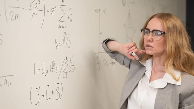 Young woman scientist writes formulas on a white board