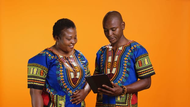 Ethnic people navigating on social media webpage, checking messages and looking at photos over orange background. African american man and woman scrolling online websites in studio.