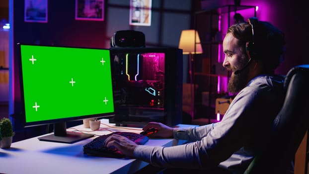 Man talking with friends online while playing together in multiplayer game on green screen desktop PC. Gamer cooperating with teammates in coop videogame using mockup monitor