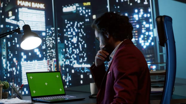 Legal investor works with greenscreen on pc at workstation, examining isolated chromakey display from panoramic view office. Chief executive director working at night with copyspace template.