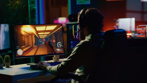 Man putting on headphones to communicate with teammates while playing first person shooter videogame with gun shooting laser bullets. Gamer talking with online friends while enjoying game
