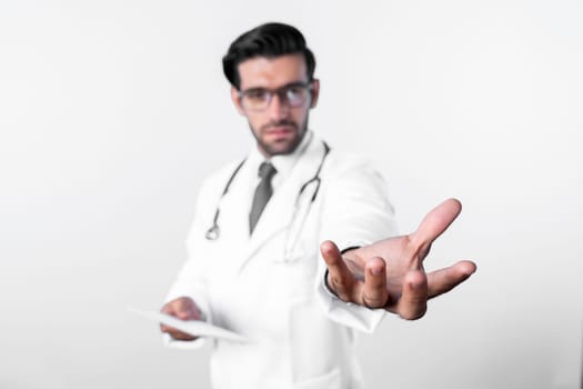 Close up of skilled doctor holding something his hands while standing at blue background. Professional smart doctor holding and wearing glasses, lab coat and stethoscope. Medical therapy. Deviation.