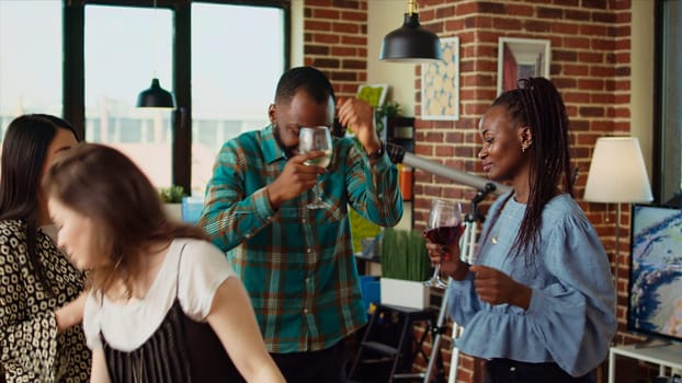 Multiracial school colleagues organizing apartment party, enthusiastically dancing to electronic music in brick wall home. Mates enjoying time spent together, busting into animated dance moves