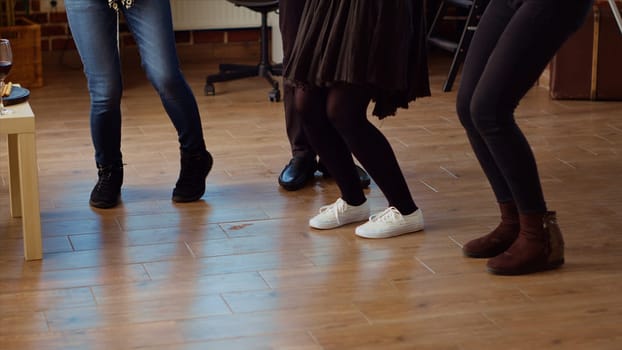 Close up shot of guests feet dancing and spinning around house during entertaining apartment party. People legs moving on energetic music rhythm, doing dance moves at social gathering
