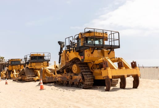 Few Yellow Crawler Dozer On Sandy Beach, Blue Sky On Background. Bulldozer Builds Roads. Construction And Landfill Equipment And Machinery. No People. Horizontal Plane. High quality photo
