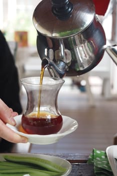 fills Turkish tea into a glass .