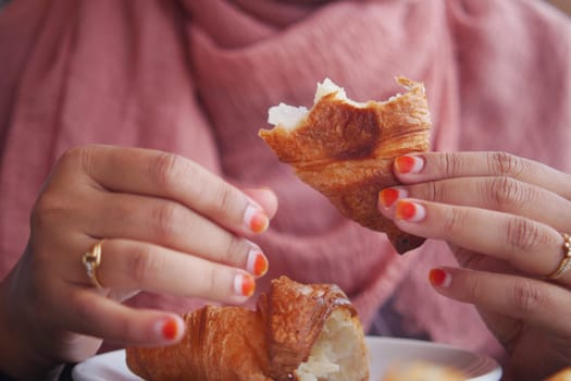 closeup of hand breaking a croissant bun .