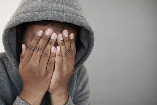 sad man in hood cover face with hands isolated in black