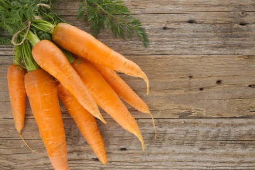 Bundle of vibrant orange carrots with green leafy tops is neatly tied together using twine and positioned on an old, rustic wooden table