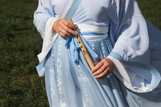 A woman in a traditional Chinese hanfu dress holds a bamboo flute close-up