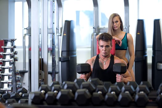 At gym. Man exercising and his girlfriend supports him