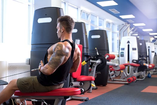 At gym. Image of tattooed bodybuilder trains on simulator