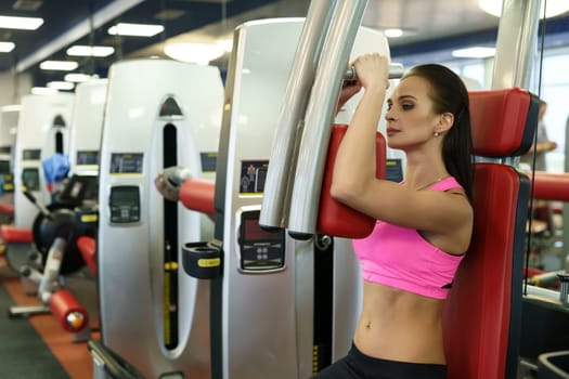 At gym. Beautiful young woman exercising on simulator