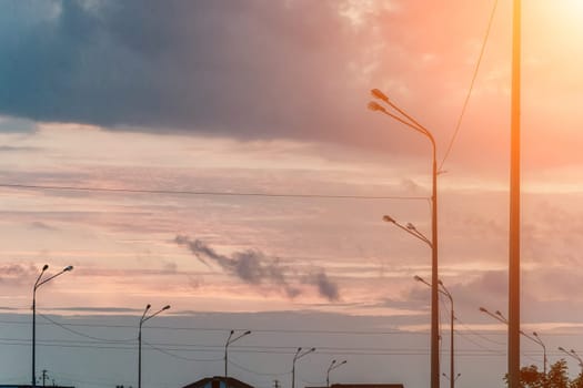 A sky with a few clouds and a street with a few street lights. The sky is a mix of blue and orange