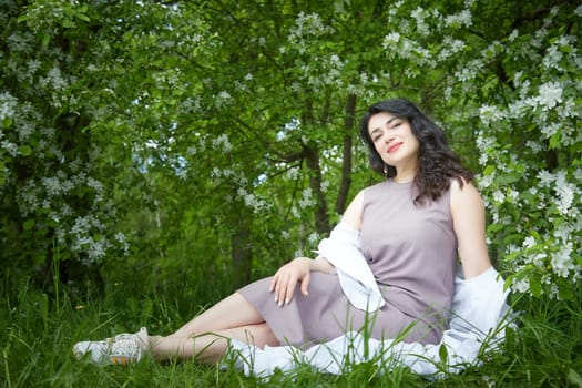 Joyous brunette woman near Blossoms of apple tree in a Spring Garden outdoors. The Concept of face and body care. The scent of perfume and tenderness