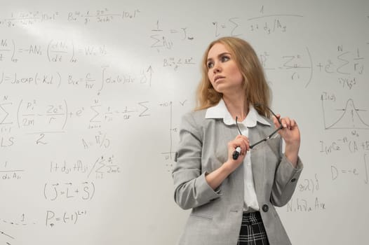 A Caucasian woman stands at a blackboard with written formulas