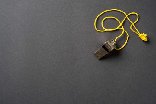 Top view of metal whistle with yellow string on dark gray background