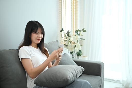 Beautiful young woman using smart phone for social media while sitting on couch.