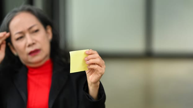 Serious middle age businesswoman sitting at office desk and reading note paper.