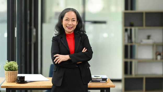 Confident mature businesswoman with financial document standing at workplace.