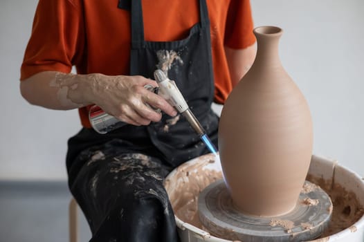 Close-up of a potter's hands firing a jug with a gas burner on a potter's wheel