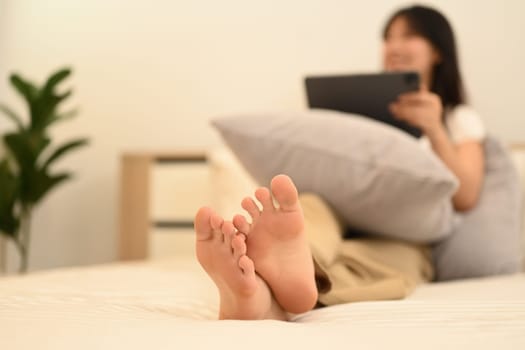 Select focus on female feet lying in bed and using digital tablet.