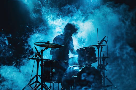 The drummer sits behind a drum kit in the smoke and spotlight.