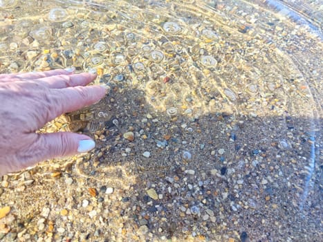 Pebbles in the water. Background, texture. Hand Disturbing Clear Water Over Colorful Pebbles. A hand touching clear water above pebbles