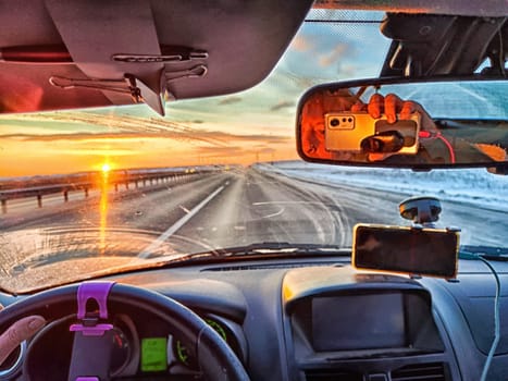 Car salon, windshield, hand on steering wheel and landscape in sunset. View from driver on nature with Road. Single traveler. Partial focus. Blurred