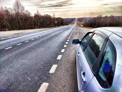 The car is on the side of the road. The concept of travel. A silver car stopped by the highway as daylight breaks