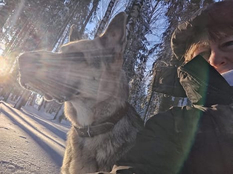 Adult girl with shepherd dog taking selfies in winter forest. Middle aged woman and big shepherd dog on nature in cold day. Friendship, love, communication, fun, hugs