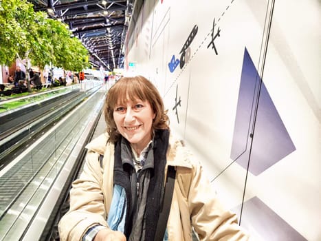 Middle-Aged Woman Taking Selfie at Airport Before Departure. A middle-aged woman captures selfie in an airy airport terminal