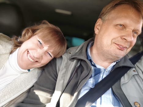 An elderly couple is happily driving through sunny countryside, enjoying their daytime road trip together