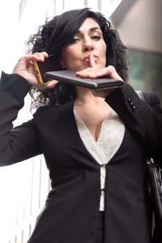 Woman with digital tablet in hand with serious face and defiant gesture with finger in mouth outdoors.Vertical