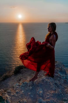 Woman sunset sea red dress, back view a happy beautiful sensual woman in a red long dress posing on a rock high above the sea on sunset