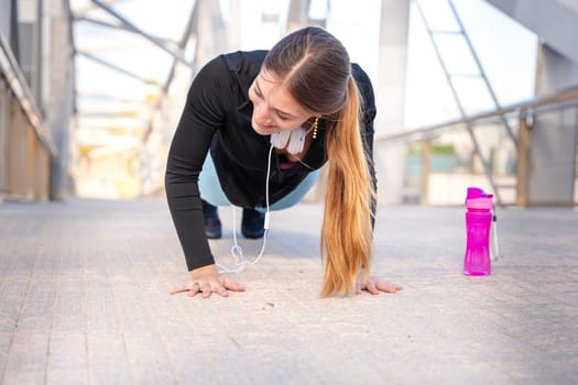 concentrated woman with sports headphones doing push-ups with sports water bottle on the floor.