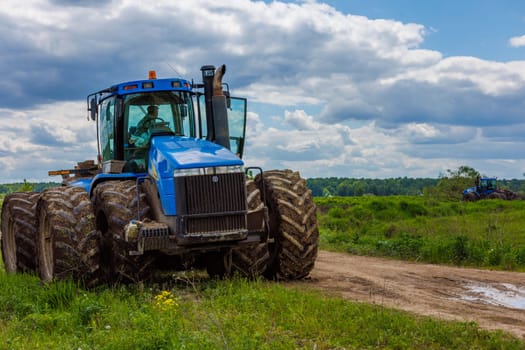 Blue New Holland tractor with double wheels standing near agricultural field at hot sunny day in Tula, Russia - June 4, 2022
