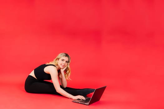 Fit woman doing stretching exercise and watching meditation video on a laptop in studio.