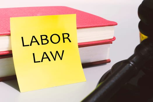 Judge's gavel with text labor law on yellow note and red books.