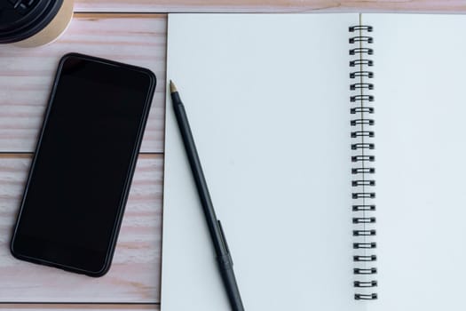 Note book with pen, smartphone and coffee on wooden desk. Directly above. Flat lay. Copy space.