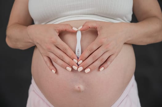 Caucasian woman holding a positive express pregnancy test against the background of her tummy