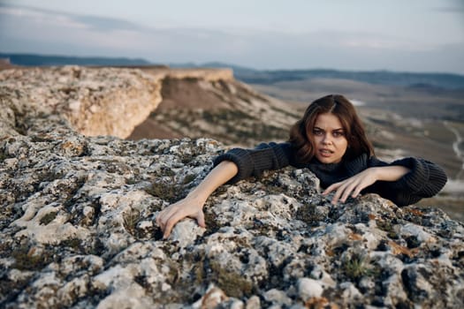 Confident woman standing in field with hands on hips leaning against rock