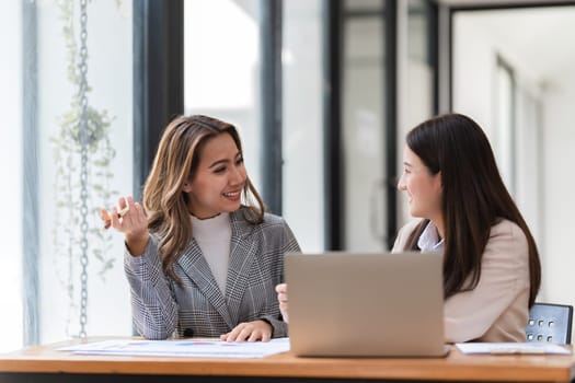 Businesswomen discussing project at desk with laptop.