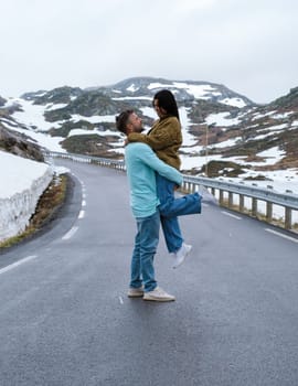 a diverse couple of men and women on a snowy road, a diverse couple at the Lyse road covered with snow to Krejag Norway Lysebotn, a road covered with snow in Spring