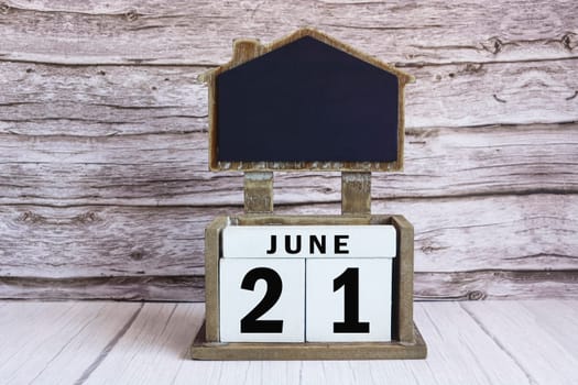 Chalkboard with June 21 calendar date on white cube block on wooden table.