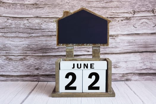 Chalkboard with June 22 calendar date on white cube block on wooden table.